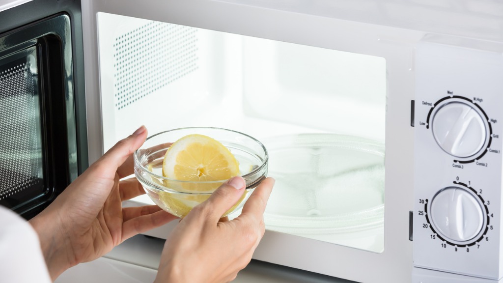 Woman putting bowl of slice lemon in microwave oven picture id928088944